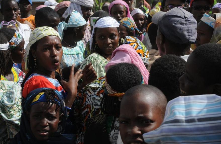 UN personnel stand near a white vehicle in a compound with fencing and trees.